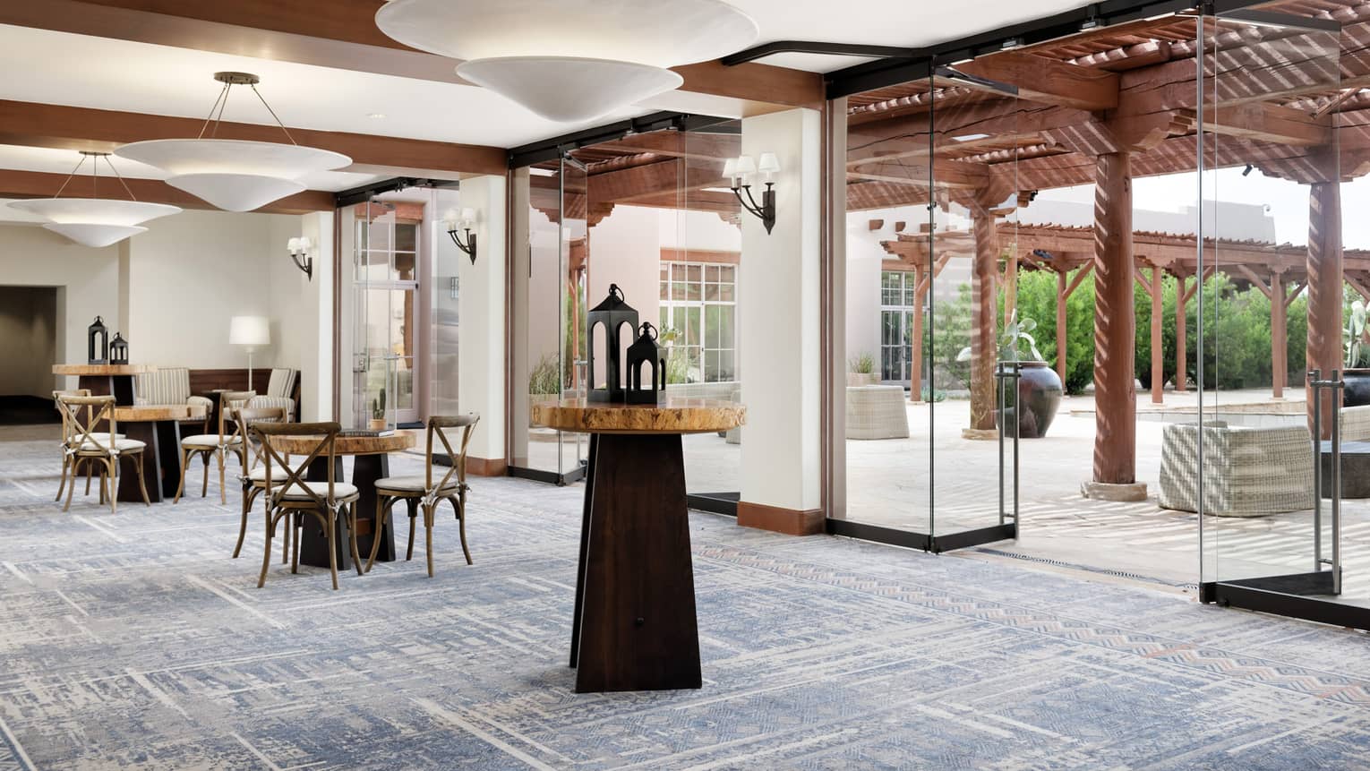 A foyer/seating area with small tables and wooden chairs, glass doors and windows cover the wall.