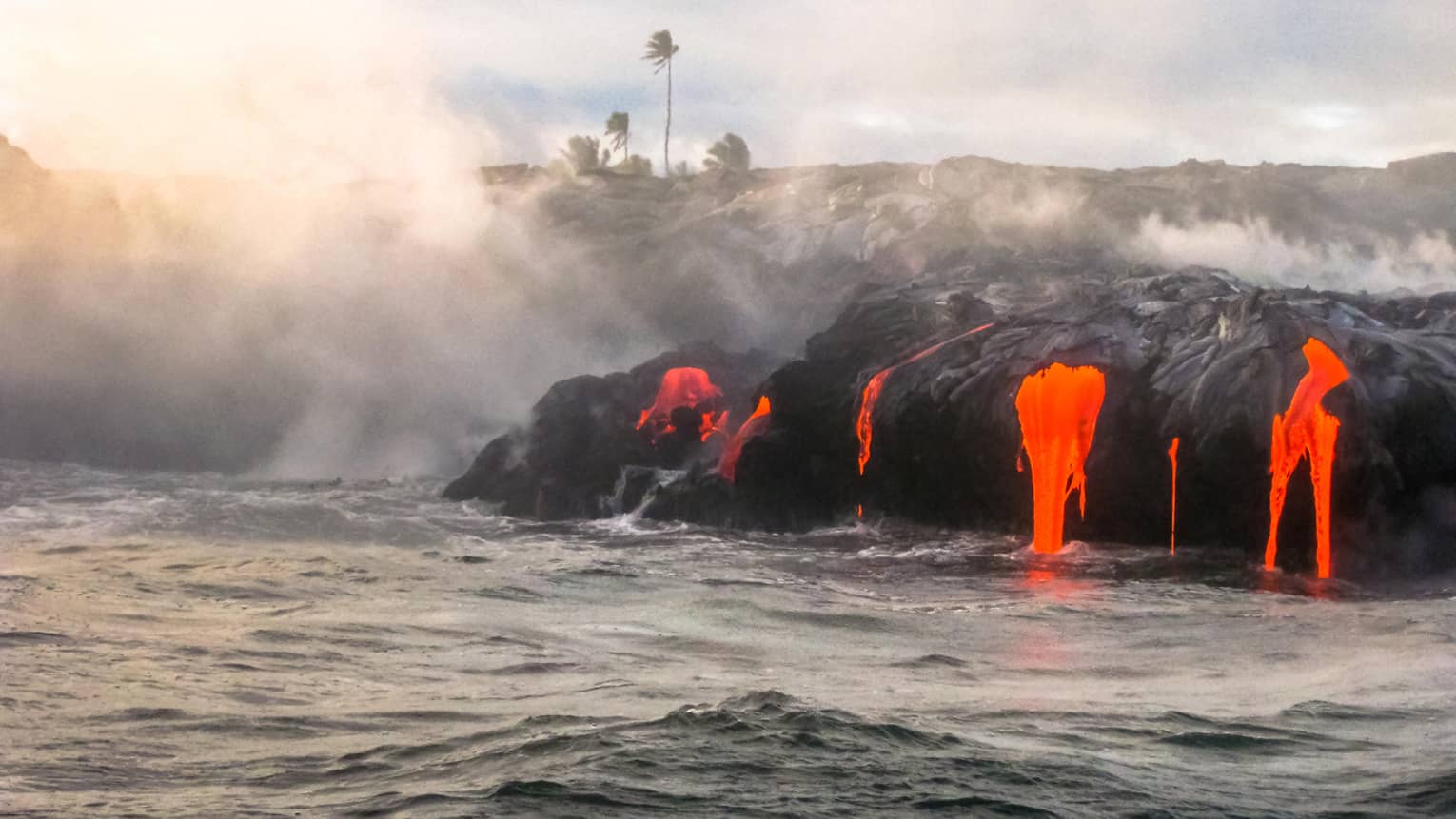 Steam rises from hot lava flowing over black rocks into ocean