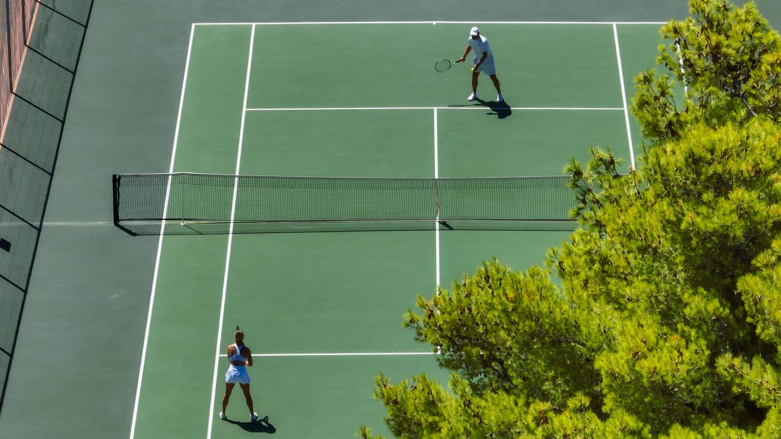 Aerial view of a couple playing tennis on green clay court