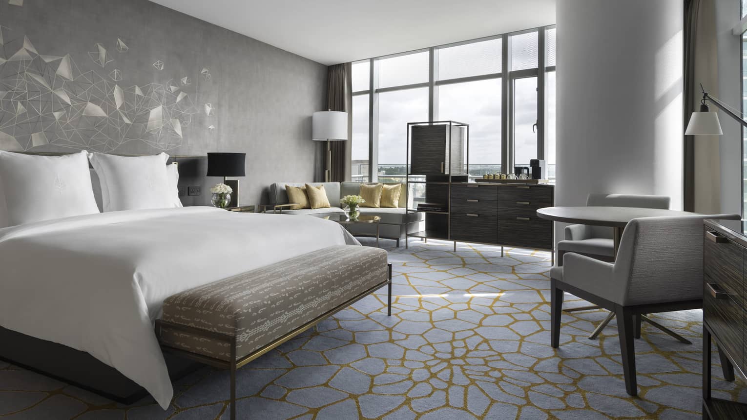 Deluxe room with queen bed, white linens, small table for 2, couch, floor-to-ceiling windows 