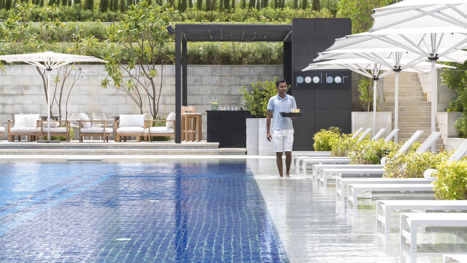 Hotel staff carries tray alongside outdoor swimming pool and sunny patio deck
