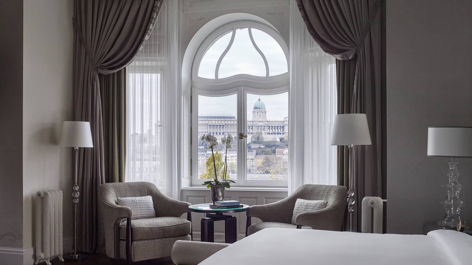 Elegant hotel room with curved window, two armchairs and a view beyond sheer curtains