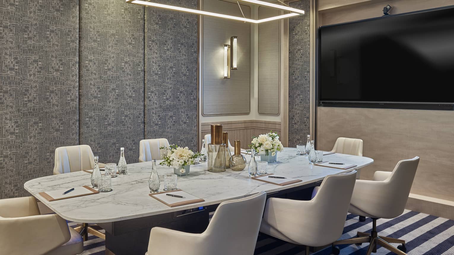 Boardroom table with eight white leather chairs, TV screen, striped carpet