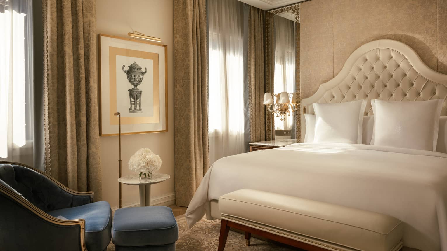 Elegant hotel room featuring a king bed with upholstered headboard and blue arm chair