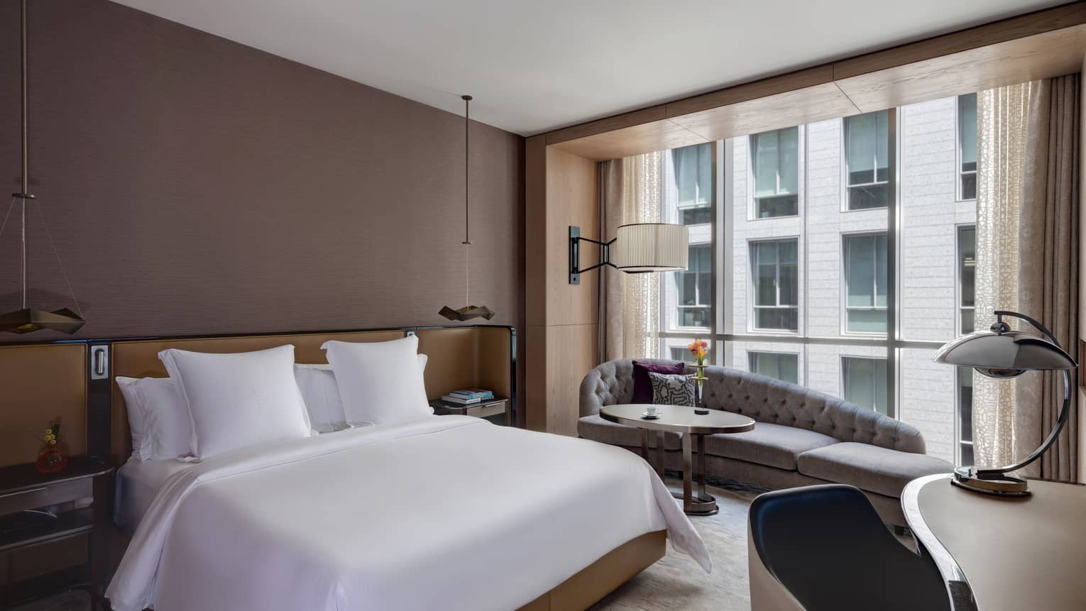 Bedroom with mauve-coloured walls, king bed and chaise by the window