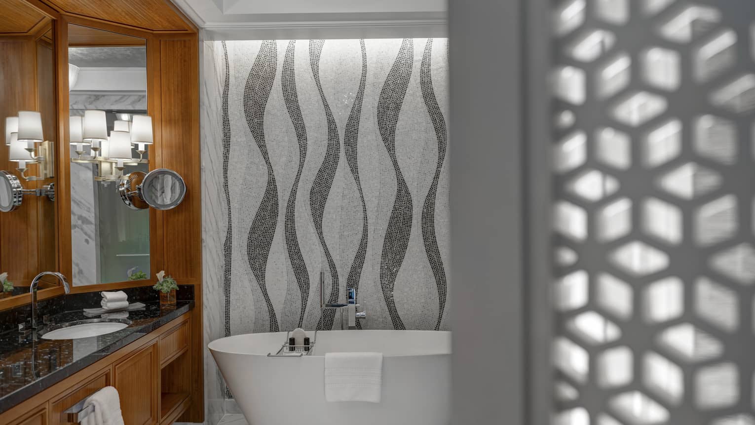 Bathroom with mosaic tiled walls, freestanding tub, vanity with black top