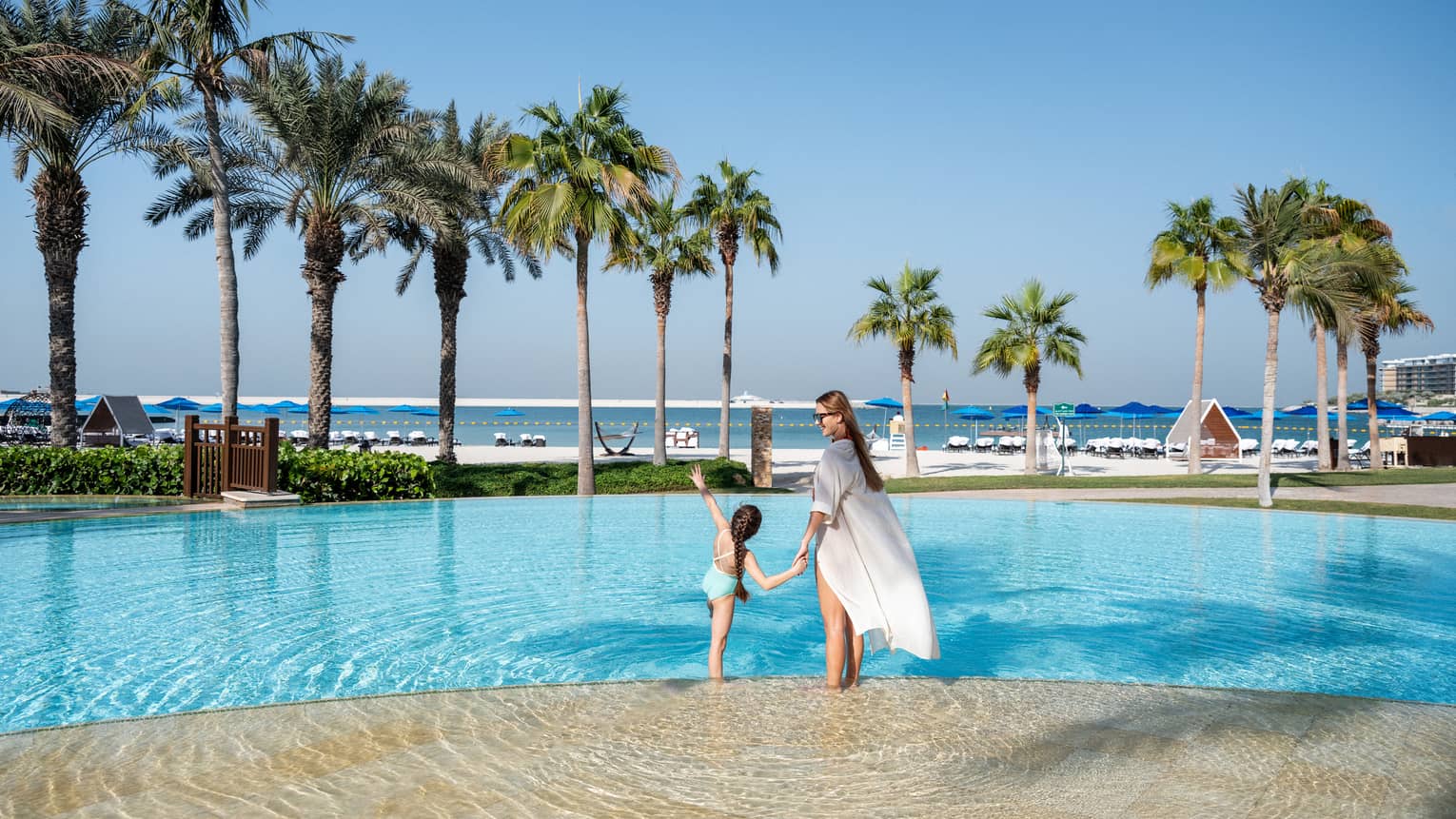A woman and a little girl hold hands while wading in the outdoor pool overlooking the Arabian Gulf