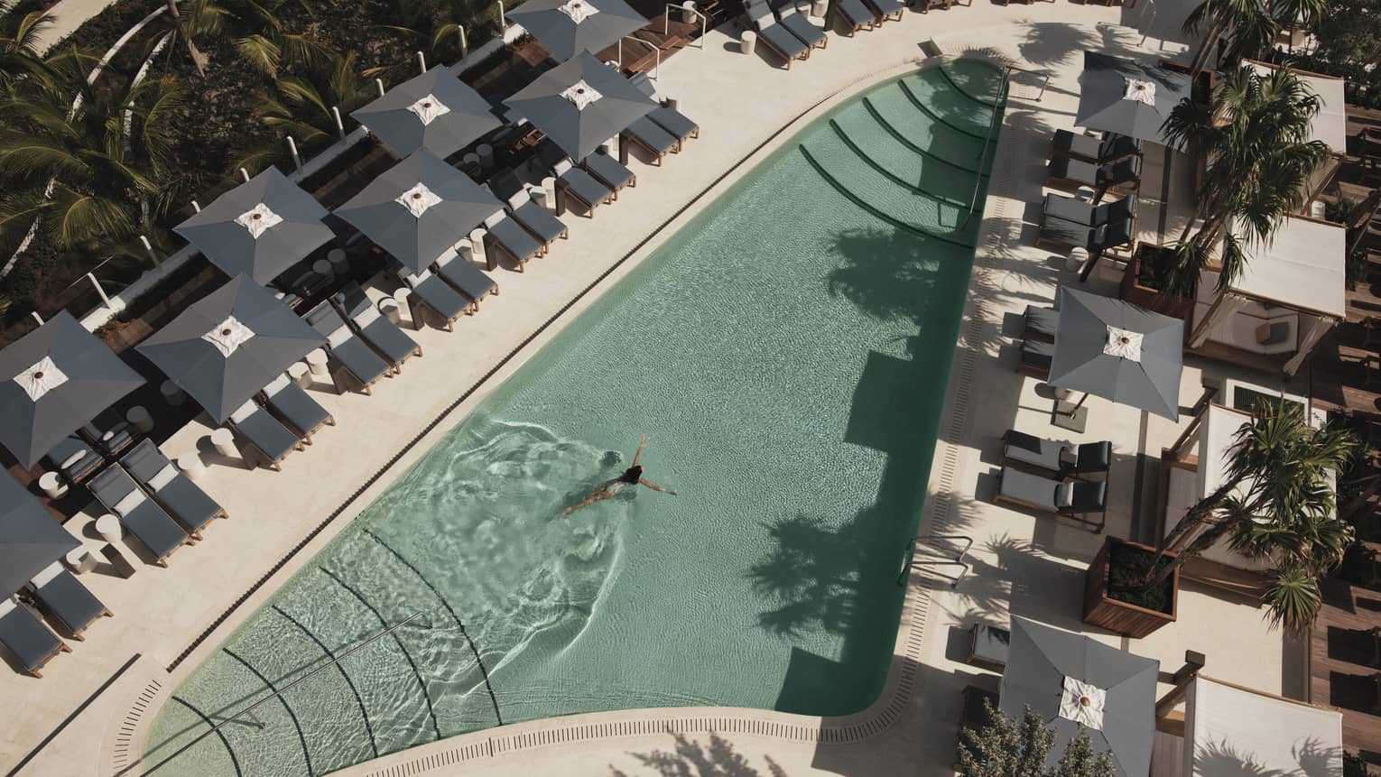 An outdoor swimming pool with grey lounge chairs and umbrellas surrounding it.