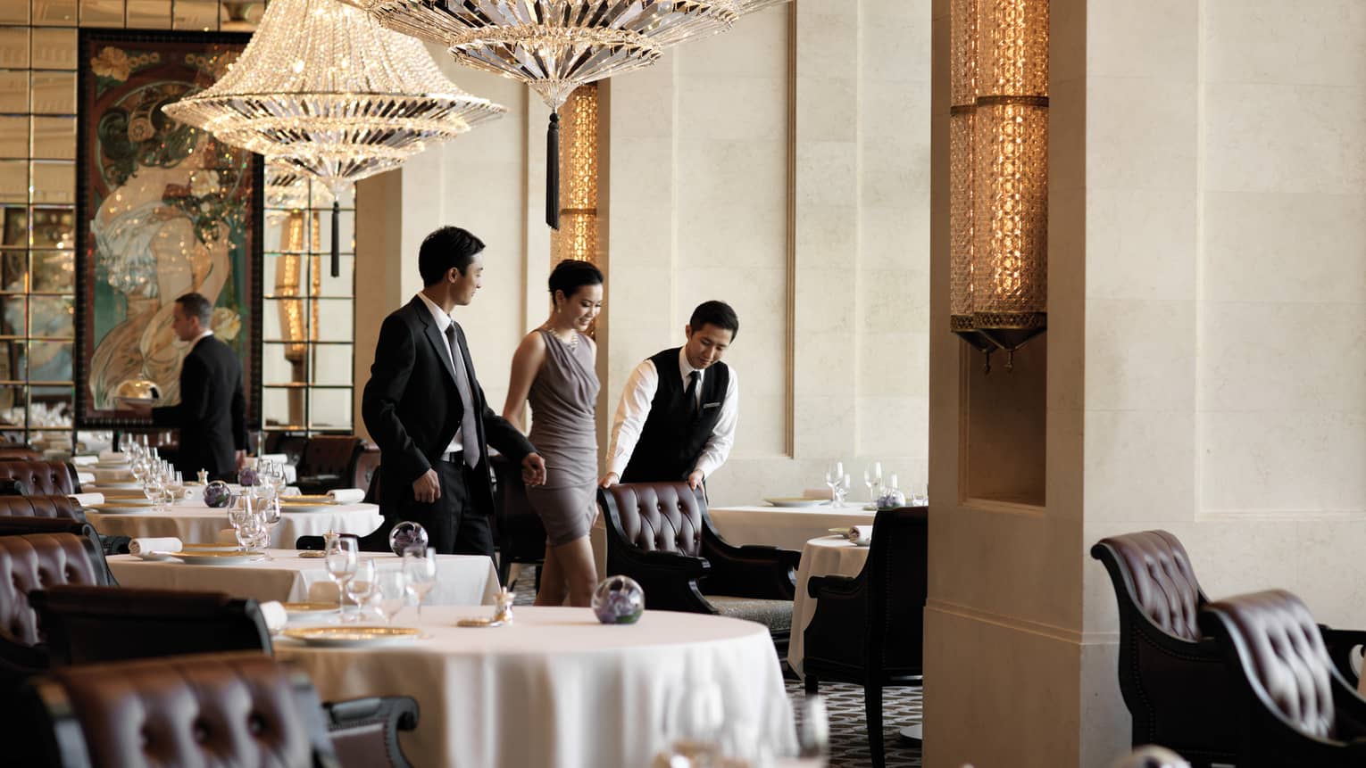 A male waiter pulls a leather seat out at a dining table for a woman