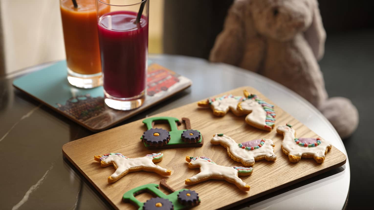 Kids tractor, unicorn and lama cookies on a wooden cutting board next to juice glasses
