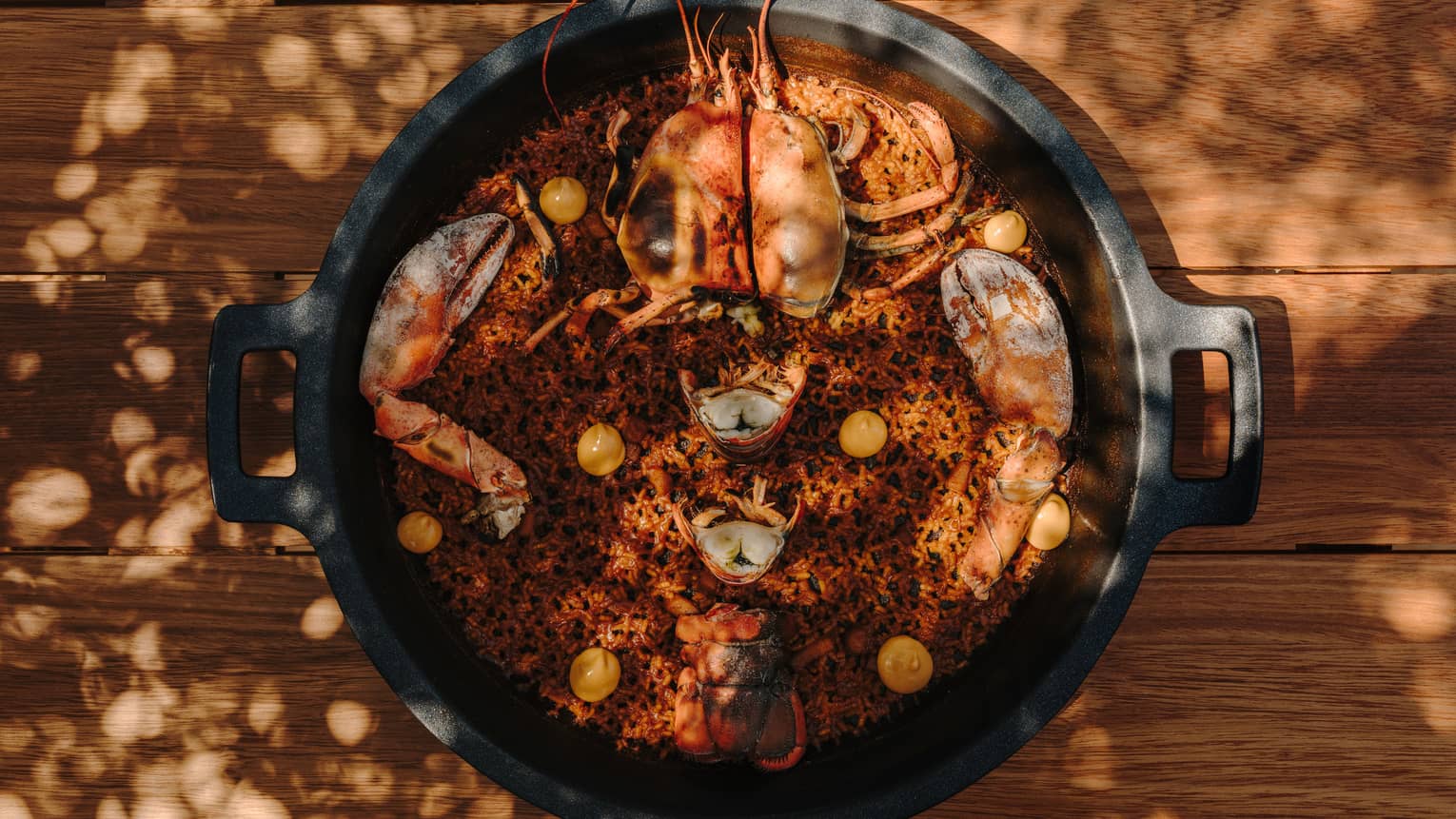 A black plate with side handles holds a rice and seafood dish.