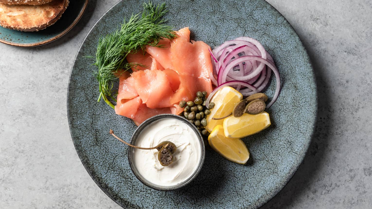 Salmon, lemon, red onion, herbs, and a white sauce on a blue plate.