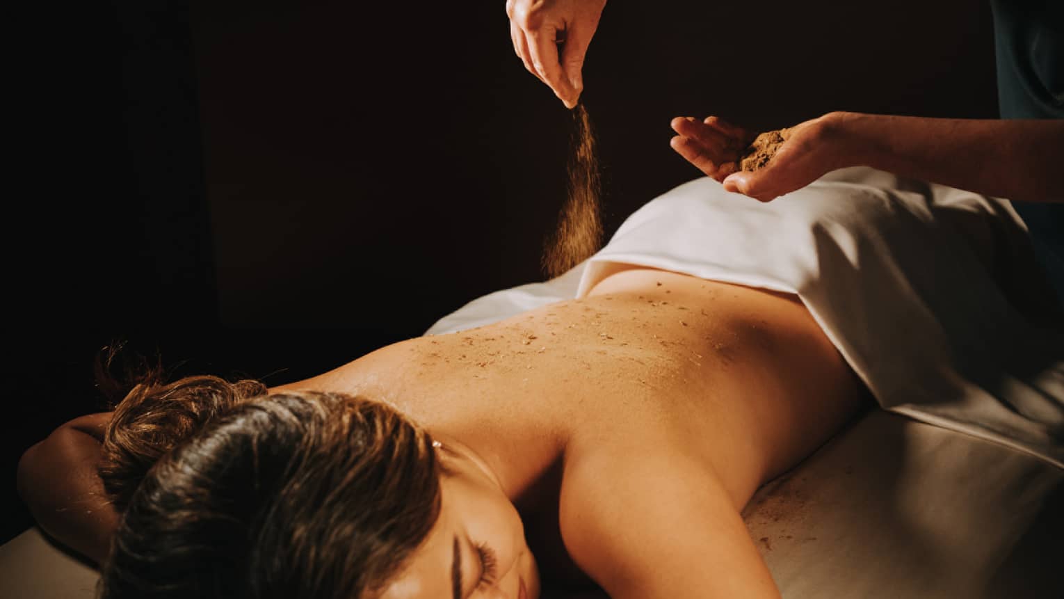 Spa staff sprinkled coffee powder over woman's bare back as she lays on massage table
