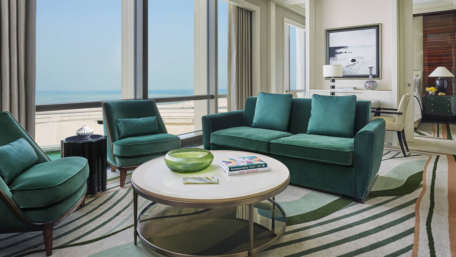 Four Seasons Executive Suite with emerald green velvet sofas, armchairs, round coffee table with books, sunny windows