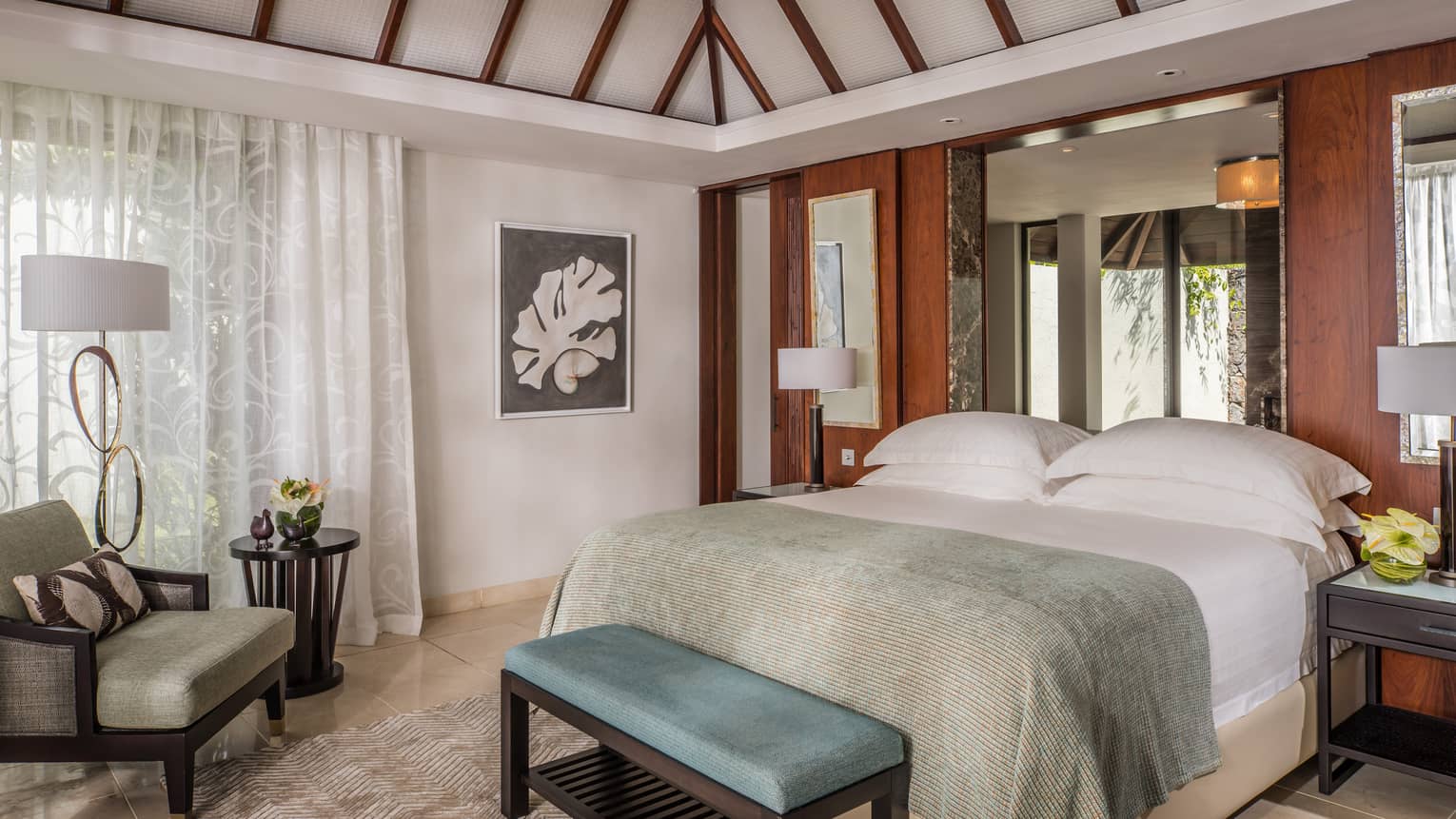 Residence Villa bed with light blue blanket, bench, armchair by drawn sheer white curtains