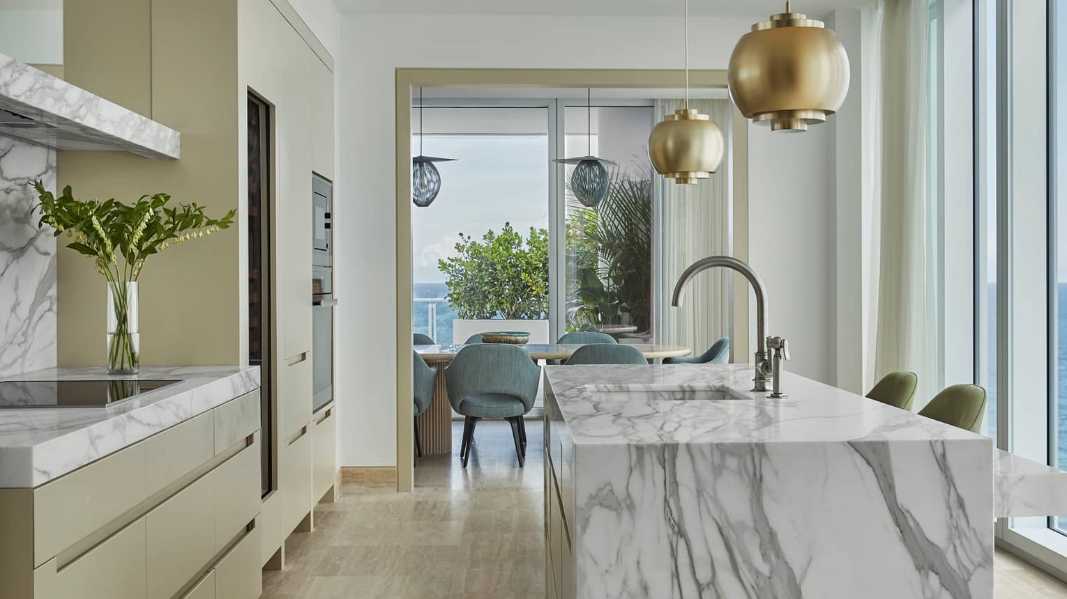 Retro-style brass lamps above grey marble kitchen island, glass wall with ocean views