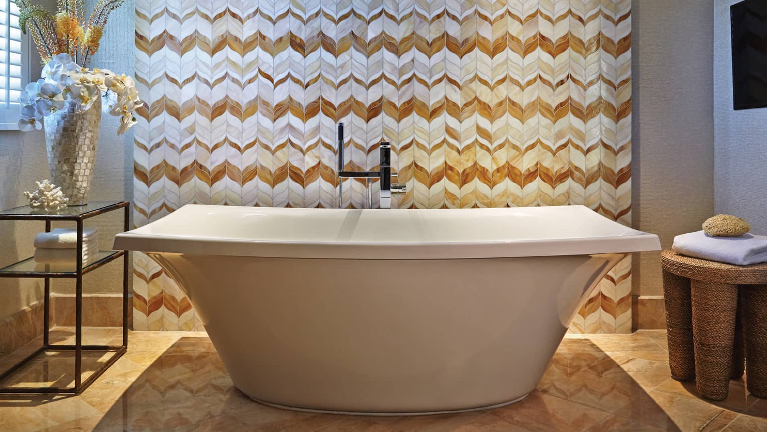 Freestanding bathtub with a modern faucet, set against a decorative chevron-tiled wall in a luxury bathroom