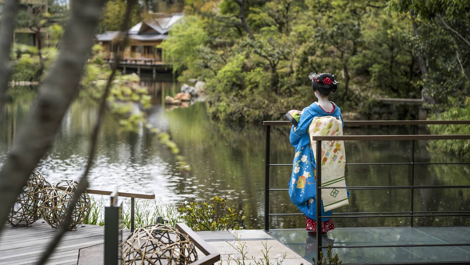 Person in a traditional blue kimono standing by a pond with lush greenery