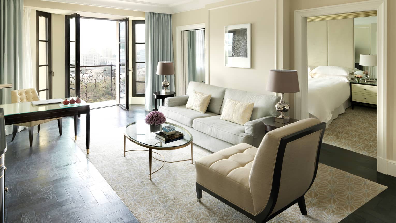 Executive Suite living room with open French doors, white sofa and plush chair, writing desk, door to bedroom