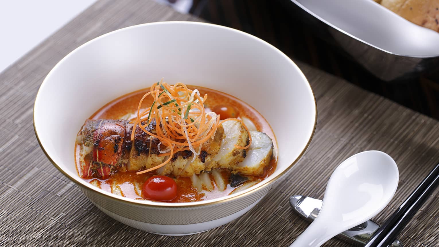 Bowl with lobster in red sauce, carrot garnish