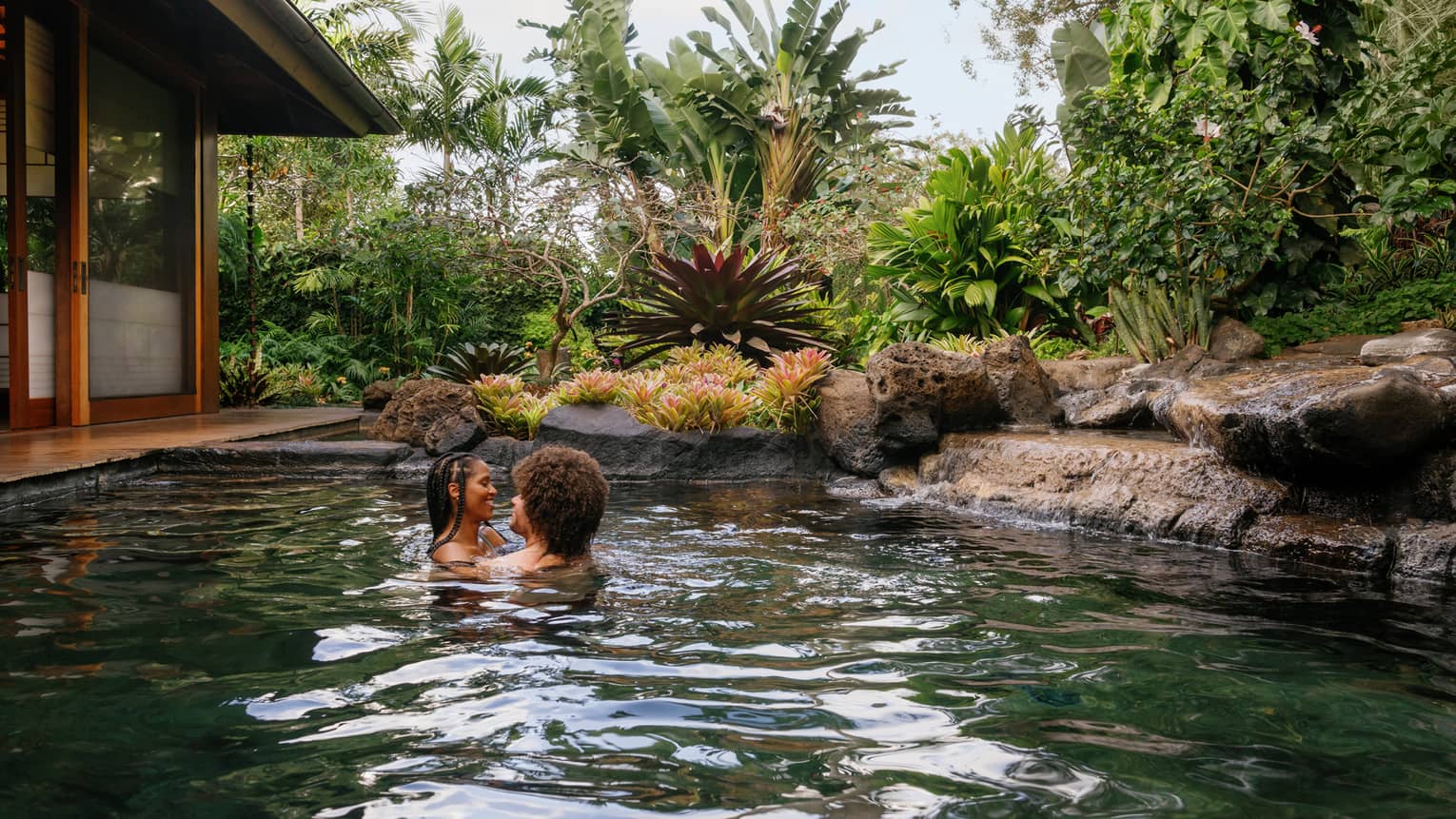 A man and woman embrace in a pond-like pool at a tropical resort