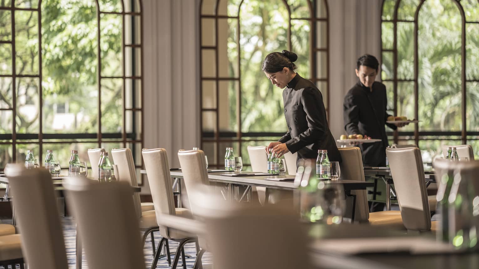 Employees placing water bottles on tables in a large classroom seating arrangement