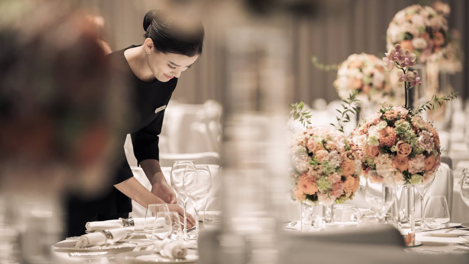Hotel server sets formal banquet table with pink roses, flower arrangements