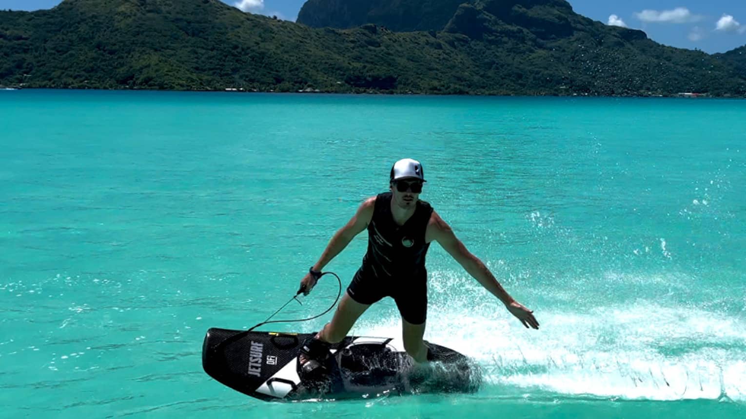 Person on JETSURF board rides on turquoise water, mountain visible in background