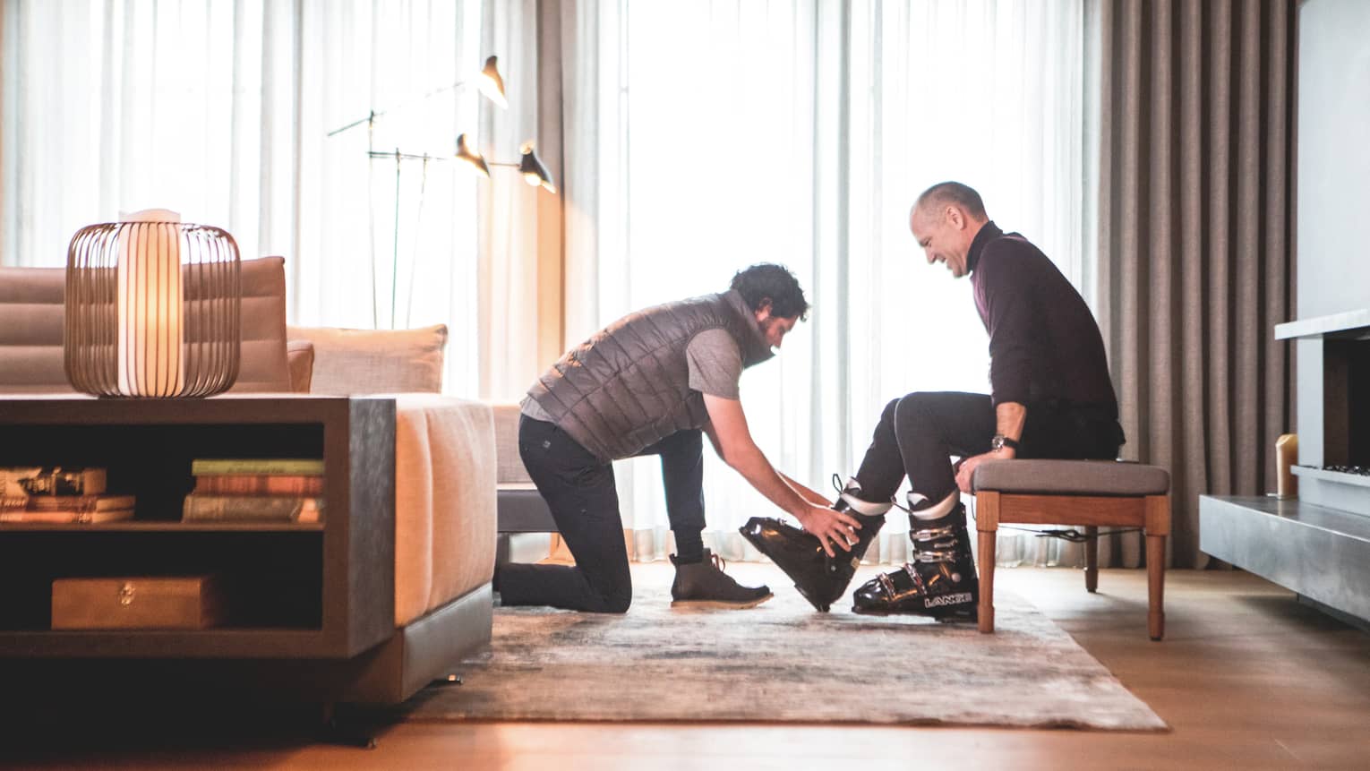 One man helping another to put on ski shoes.