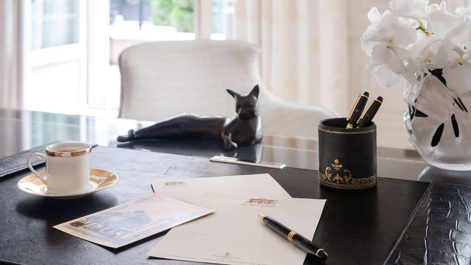 Royal Suite writing desk with pen and paper, gold-rimmed coffee cup, black cat statue 