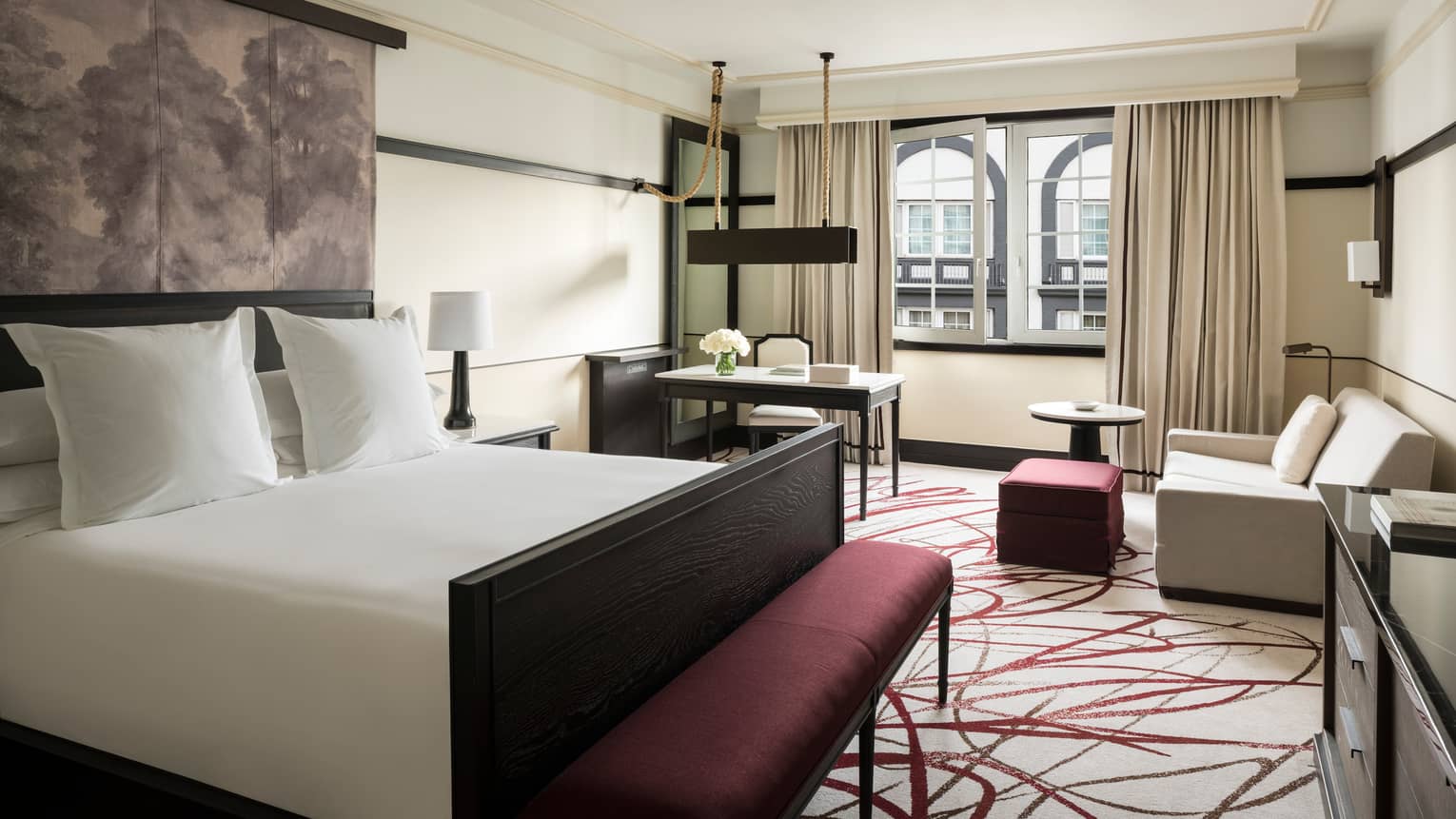 Deluxe Room bed, padded printed headboard, purple bench at foot, sofa and desk by window
