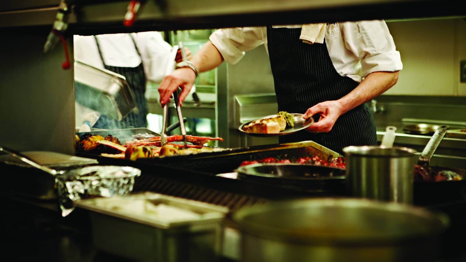 Close-up of restaurant grill, chef holding tongs and plating large fish filets