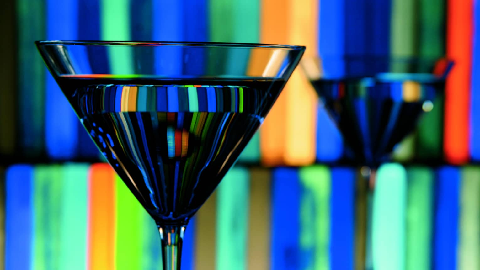 Colourful lasers, lights on wall behind martini glass, reflected in cocktail