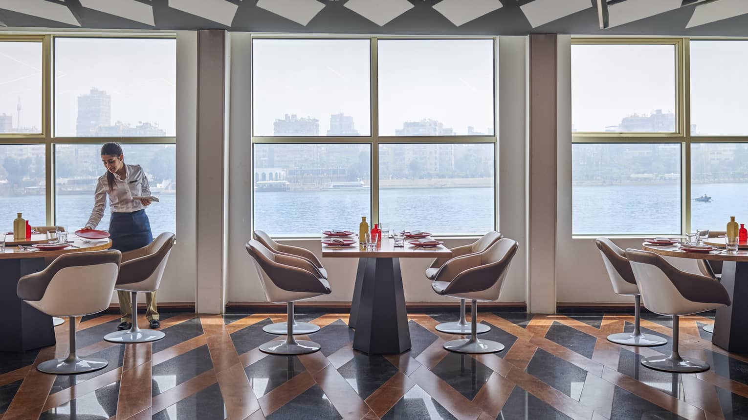 Contemporary restaurant with server on left, rectangular tables, lattice floor, Nile River views