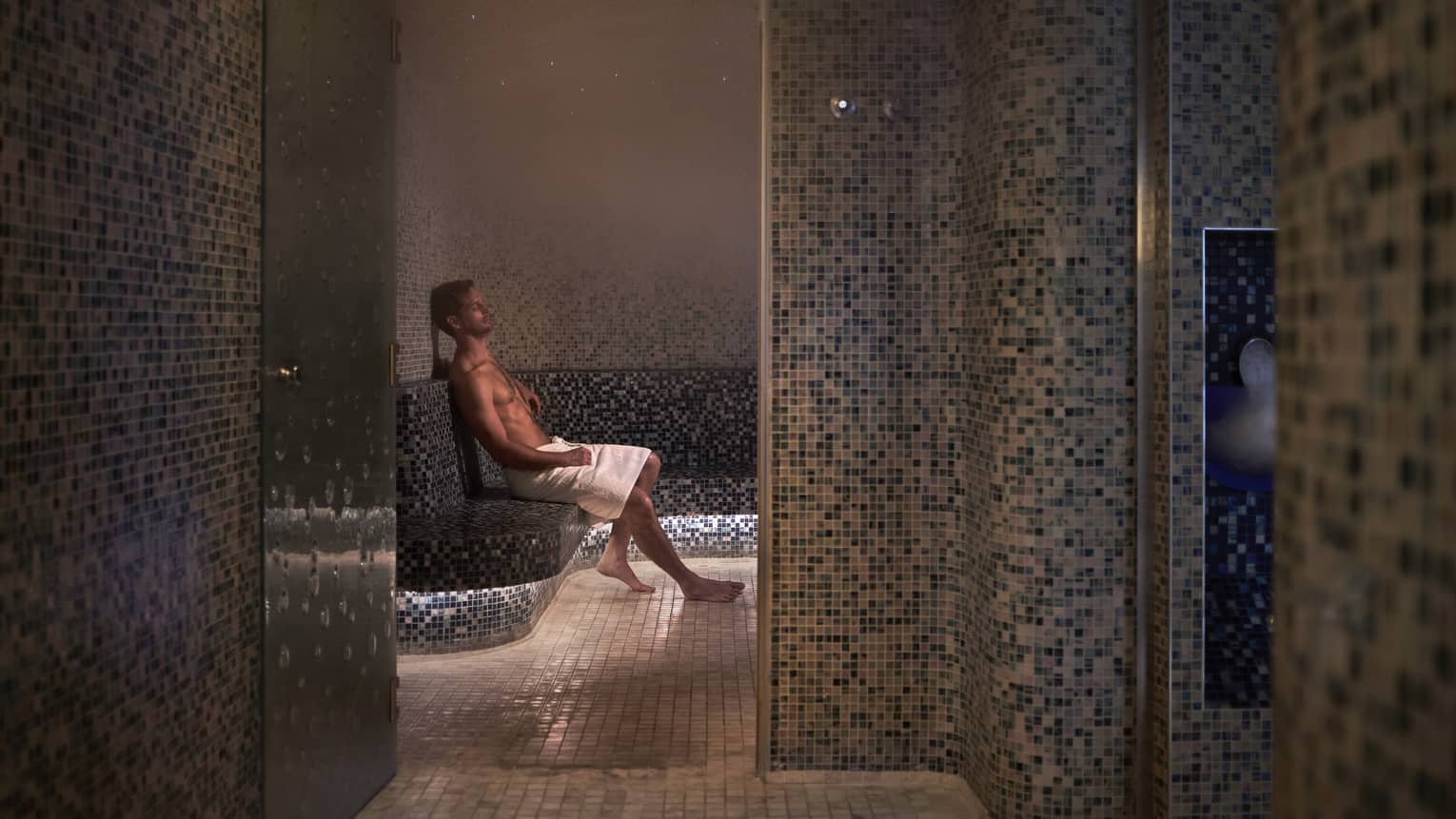 A man sitting with a towel in a dimly lit spa room.