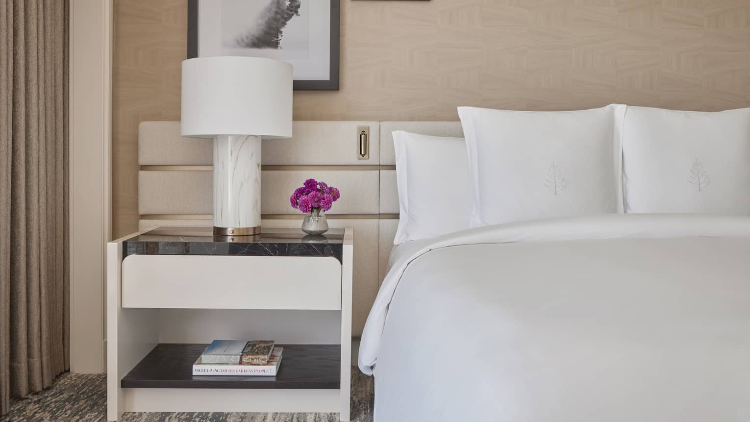 A bed in a studio room with a side table and lamp.