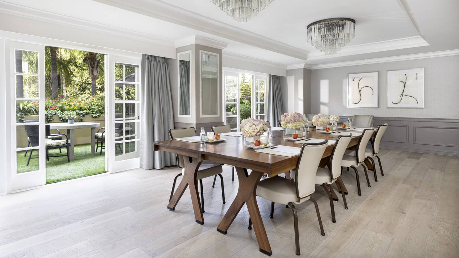 A meeting room with long wooden table, beige chairs and open patio doors.