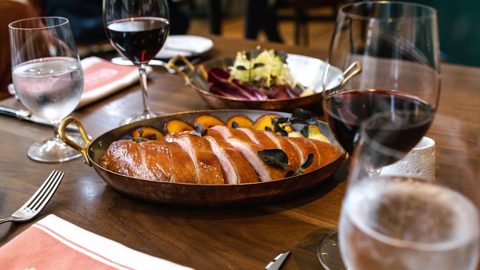 Table set with Whole Rotisserie Duck sliced in a cast-iron pan along with two wine glasses and silverware