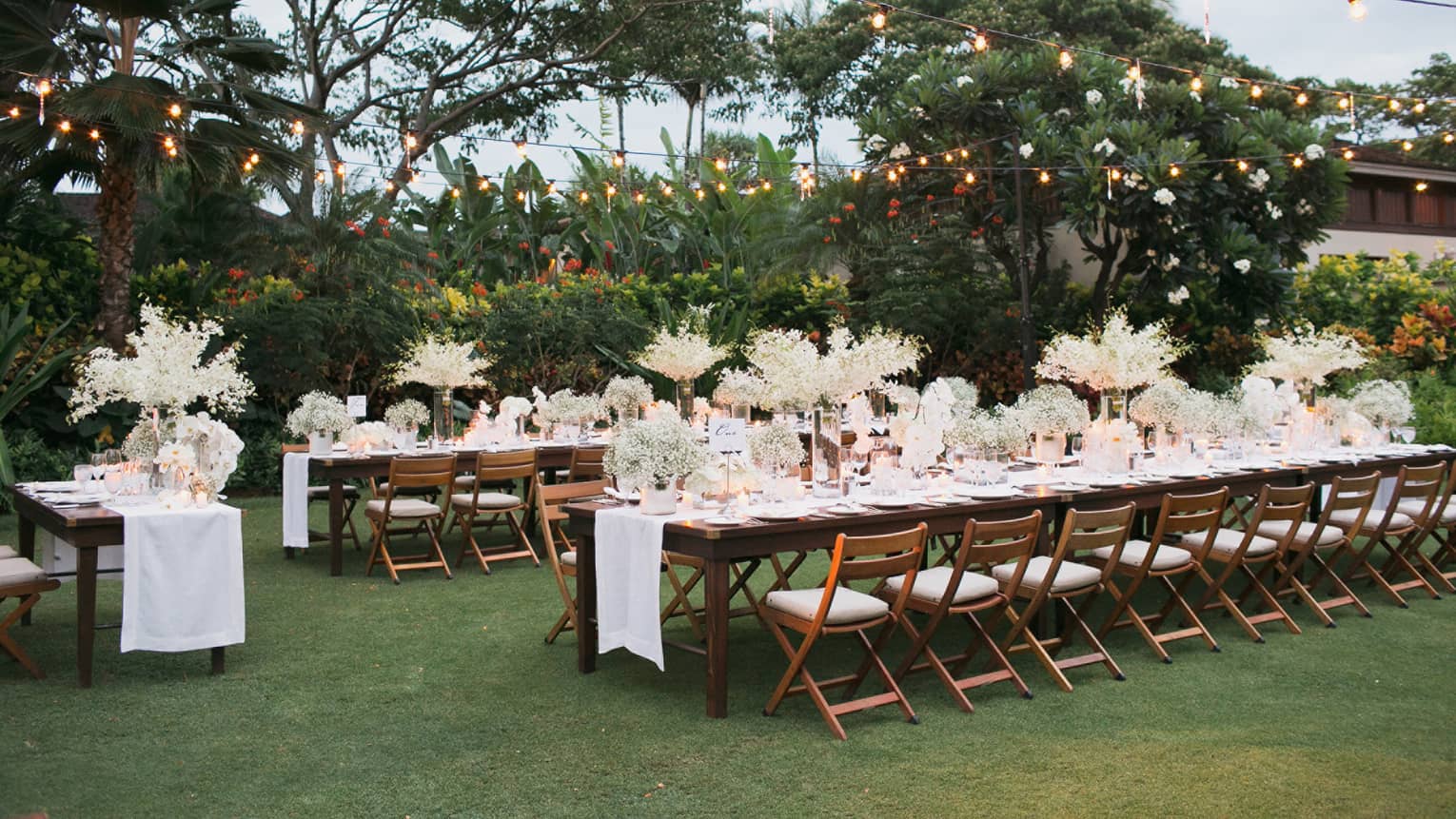 Rows of outdoor wedding reception dining tables with white flowers on event lawn