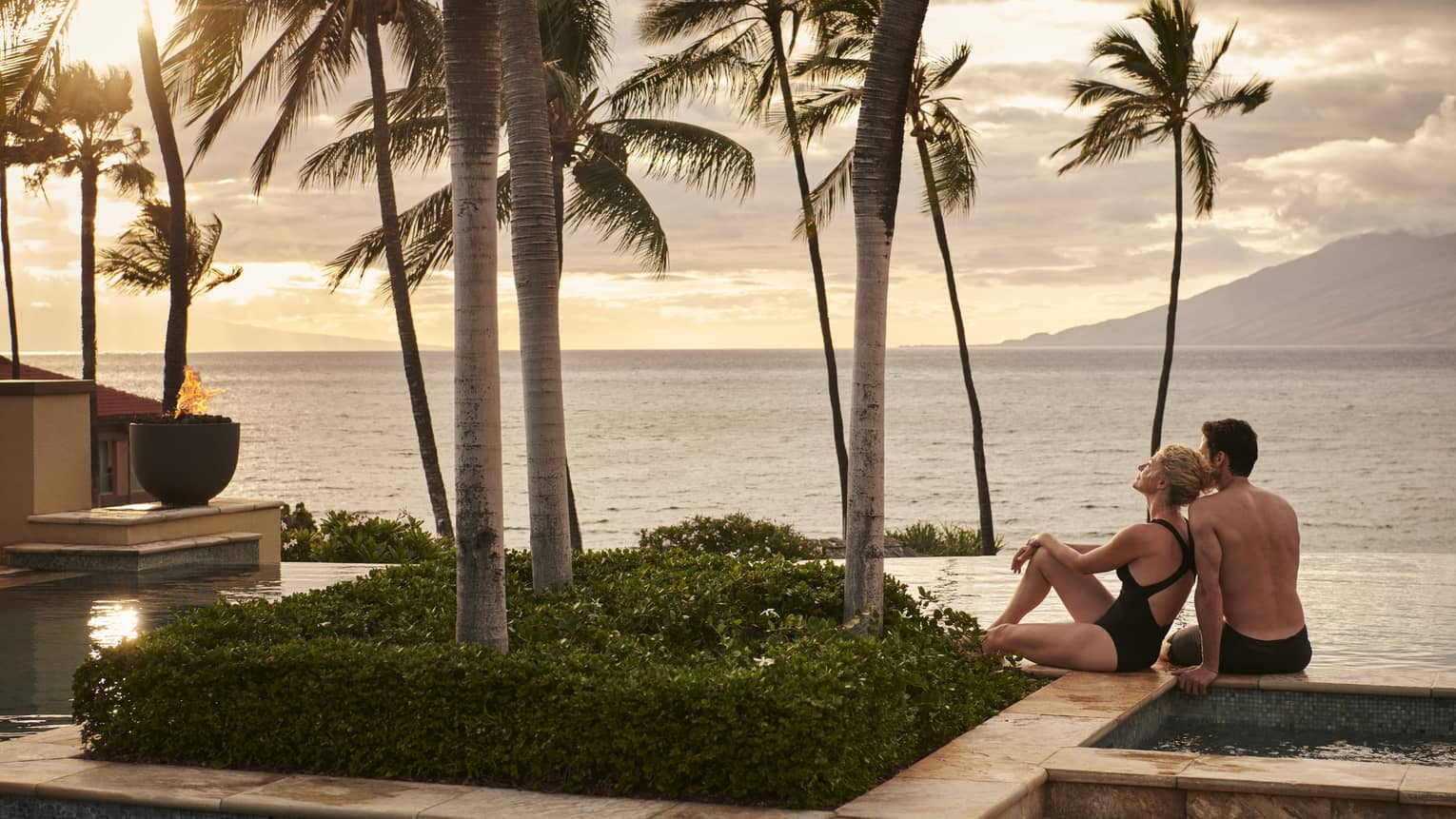 Man and woman lounge at pool's edge overlooking ocean in Maui