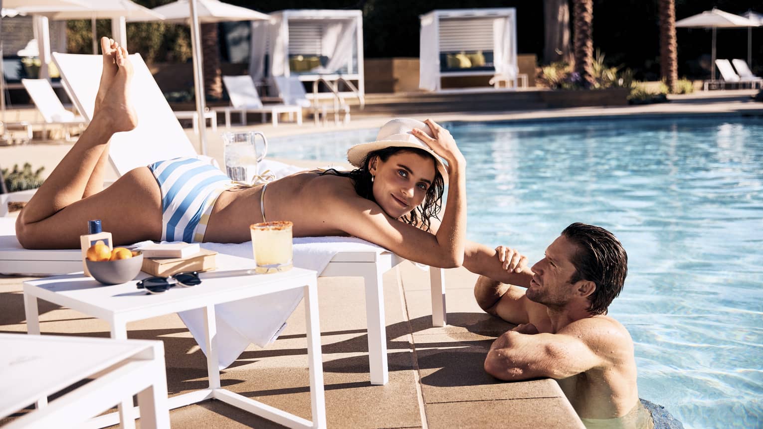 Guest laying in a lounge chair by the pool while the other guest stands in the pool.
