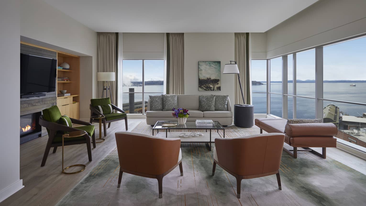 Living room with sofa, four chairs, fireplace and TV, chaise and wrap-around windows looking out to Seattle seafront