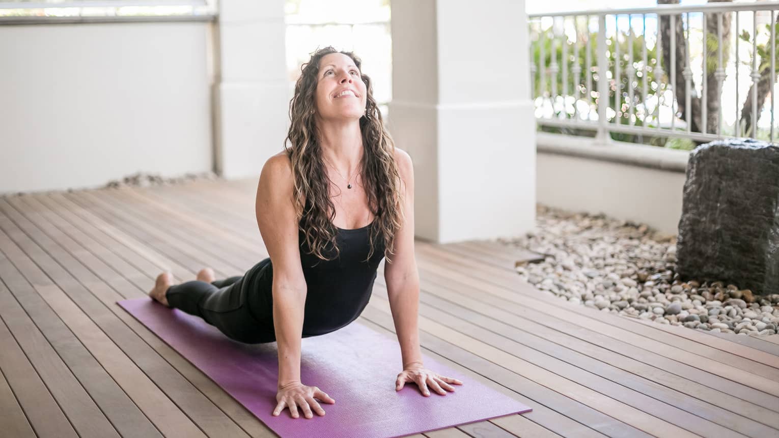 Woman smiles, looks up as she does yoga stretch on all fours on purple mat 