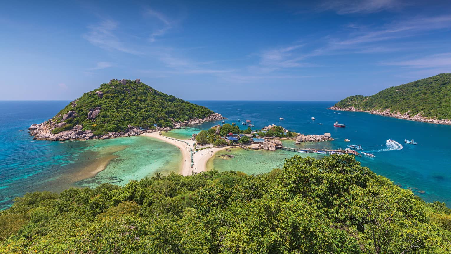 View over lush tropical trees, mountains to white sand beach and ocean below