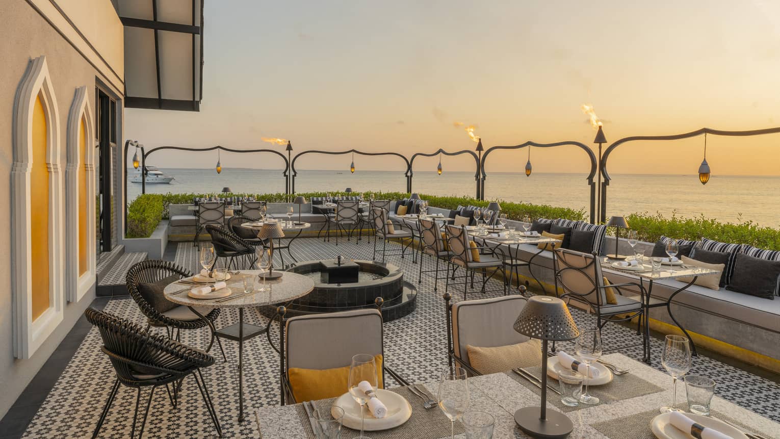 Outdoor terrace of Al Barakat at sunset with round and square tables, rattan chairs, string lighting