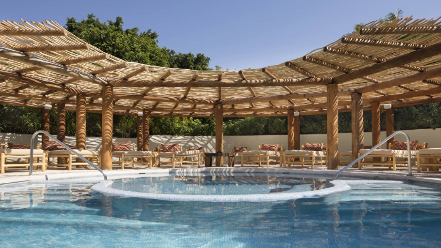 Resort pool with two entries and lounge chairs under thatched-roof awning