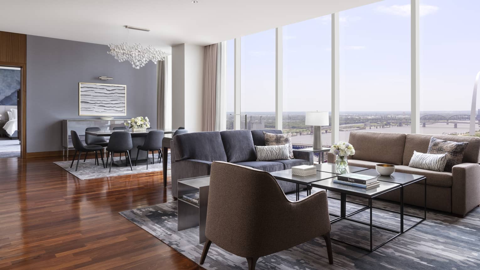 Suite living and dining area with two sofas, armchair, coffee table, dining table with chairs and large windows offering a view of the Gateway Arch and river