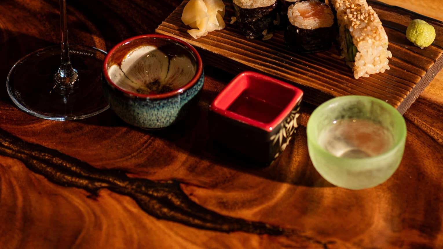 A glass of sake paired with sushi served on a wooden plate with decorate ceramic bowls