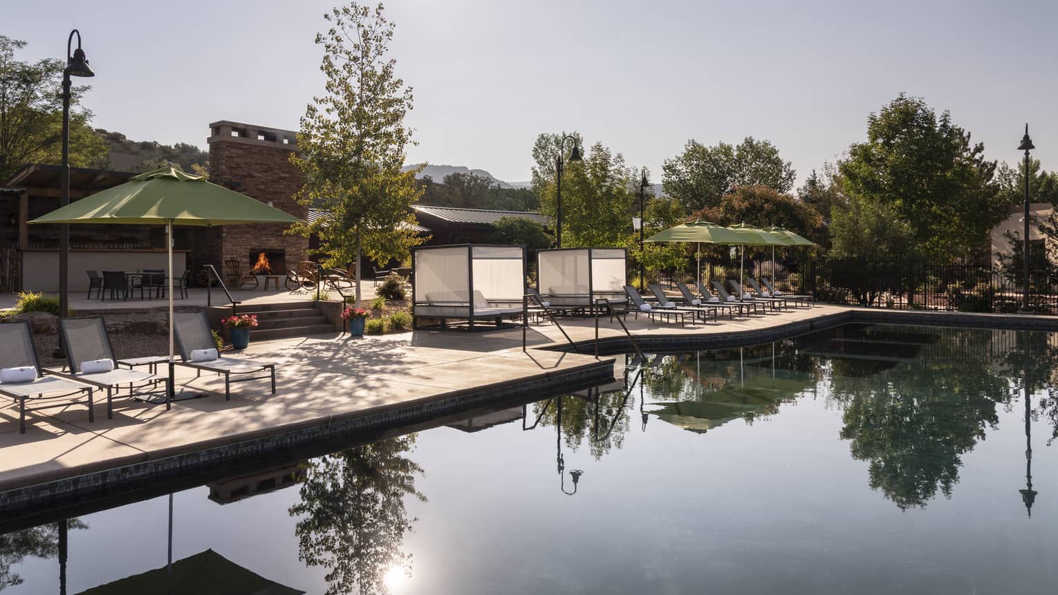 An outdoor pool near trees, lounge chairs, and green umbrellas.
