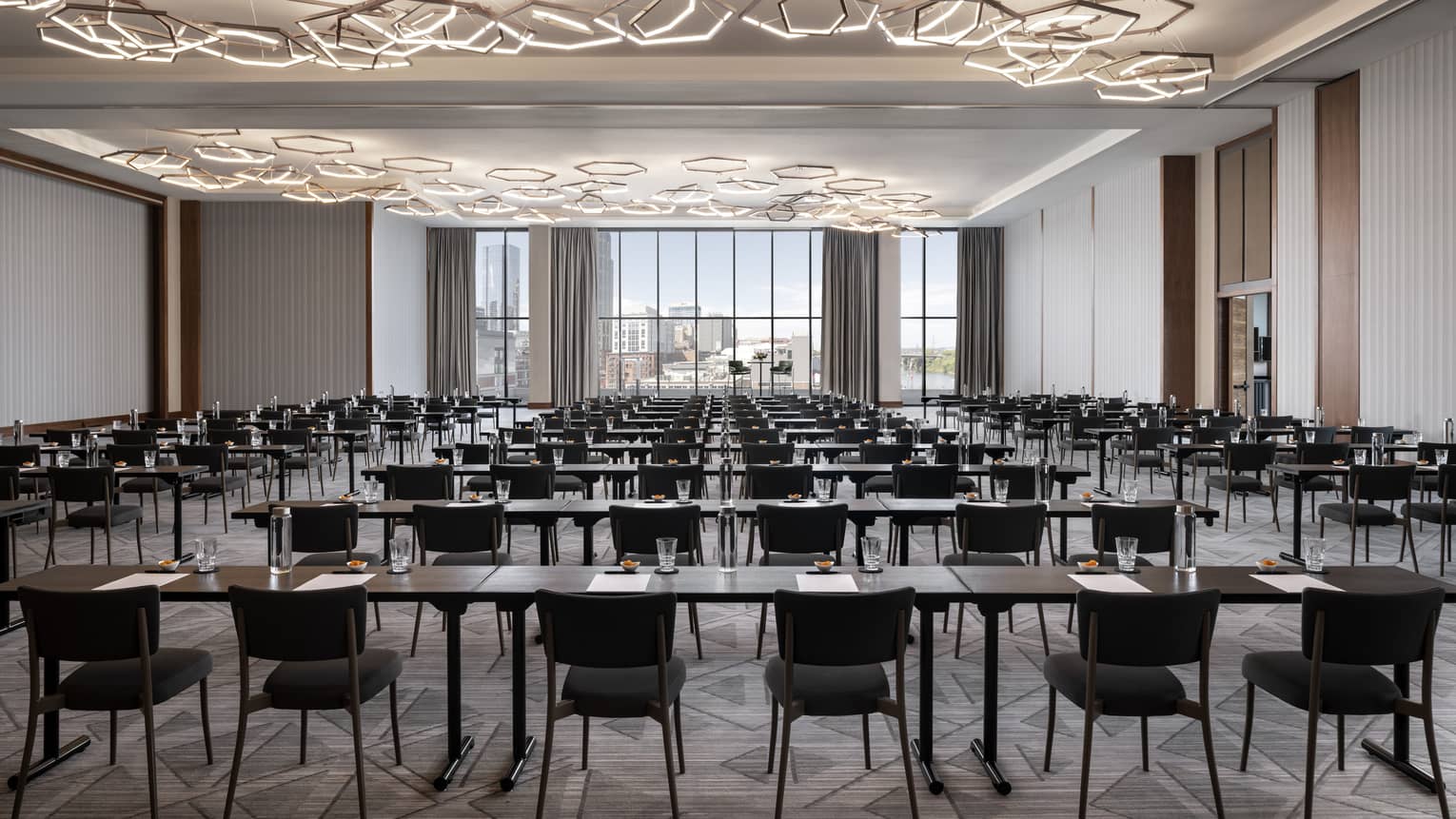 A large meeting room with many tables and chairs, geometric lights and large windows.